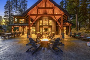 Dramatic timber lodge with glowing fire pit and expansive twilight patio lounge.