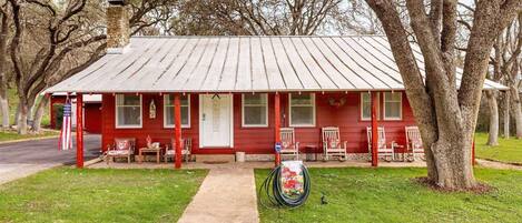 River Road Retreat is a charming red farmhouse with a classic tin roof and a welcoming front porch adorned with rocking chairs.