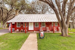 River Road Retreat is a charming red farmhouse with a classic tin roof and a welcoming front porch adorned with rocking chairs.