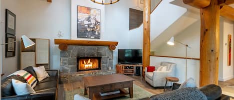 Living room with a large stone surround wood burning fireplace, and TV.