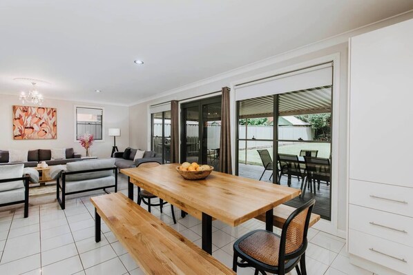 The light and airy dining area includes an eight-seater setting where guests can enjoy meals together, with glass doors opening out to the deck.  
