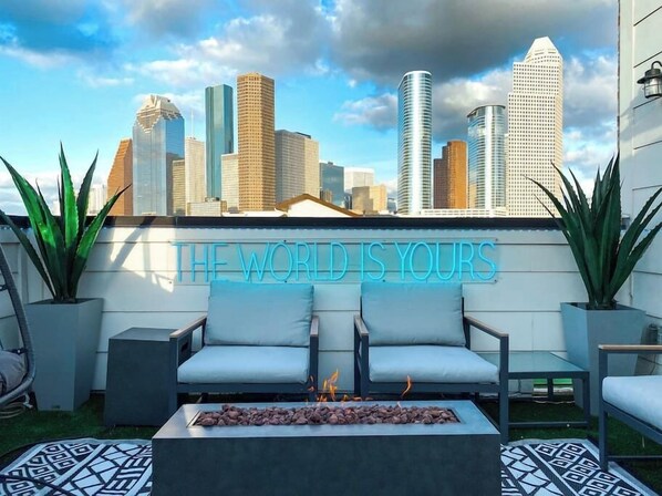 Large rooftop deck with stunning views overlooking downtown HTX. Features a fire place, custom neon sign, 3 seater sofa, 2 seater love seat, 2 single chairs, and one suspended egg chair.