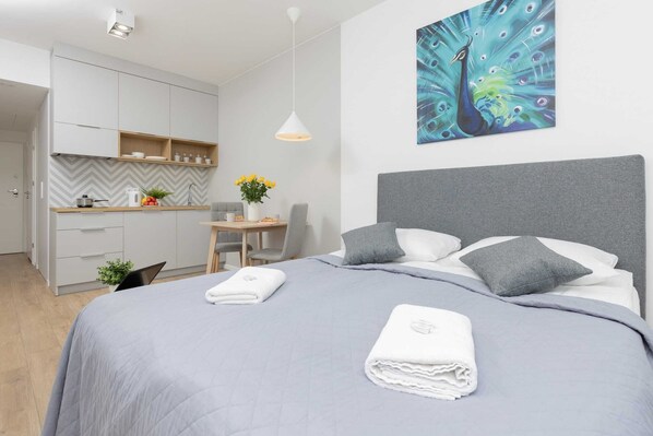 The studio features a comfortable double bed with light gray bedding and a decorative pillow. A modern painting hangs above the bed, adding a stylish touch.