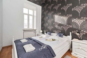 A well-lit bedroom featuring a spacious double bed with soft linens and a striking wallpaper behind the headboard.