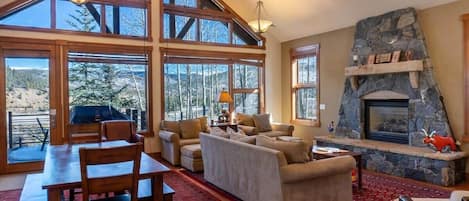 The stunning open-concept great room boasts soaring windows, a beautiful stone fireplace, and exposed wood beams featured throughout the space.