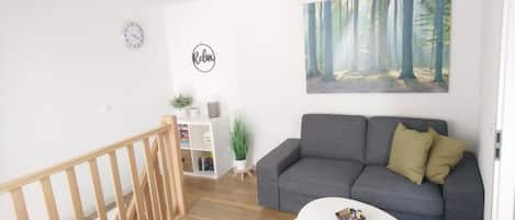 Wohnzimmer mit 2-Sitzer-Sofa, Sessel, Fernseher und Arbeitsplatz