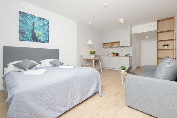 The sleeping area includes a comfortable double bed with gray bedding and a large window providing natural light and a view of the greenery outside.