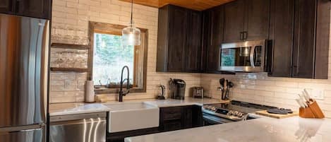 The newly-remodeled kitchen features sleek modern touches, like open shelving, tile backsplash, and stainless steel appliances. It also boasts a coffee maker, toaster, and blender.