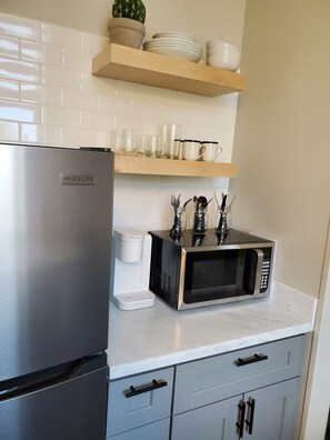 Kitchen with microwave, Keurig, glassware, flatware, coffee cups.