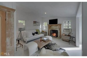 Open living area w/ painted wood floors, white walls, rustic stone fireplace.