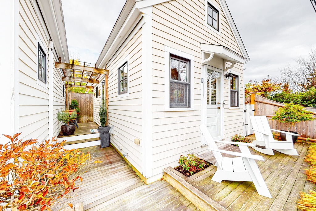 A white cottage vacation rental in Cape Cod is seen with ample outdoor space and autumn foliage surrounding white Adirondack chairs