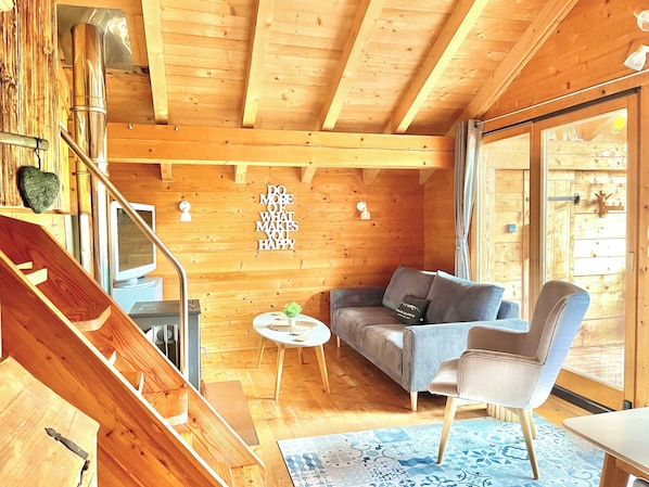 Salon avec poêle à bois, baie vitrée donnant sur la terrasse où il y a le sauna 