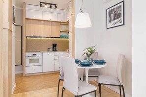 A compact kitchen with light wood cabinets, white dining chairs, and modern appliances, maximizing space and functionality.
