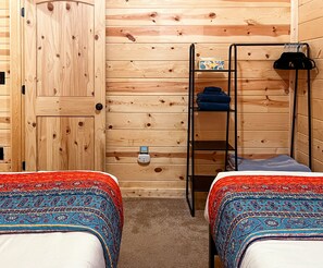 Classic log cabin designed room w/ 2 twin sized beds. Offers rack with shelves.