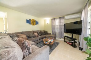 The living room space feature a 65" smart TV, sound bar, coffee table, and games