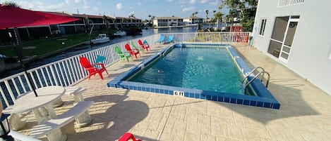 Pool overlooking canal with lots of seating, table with umbrella and more.