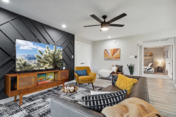 Living Room. Faux leather sofa, mustard sitting chair, clear coffee table, 65" Smart TV w/ Streaming