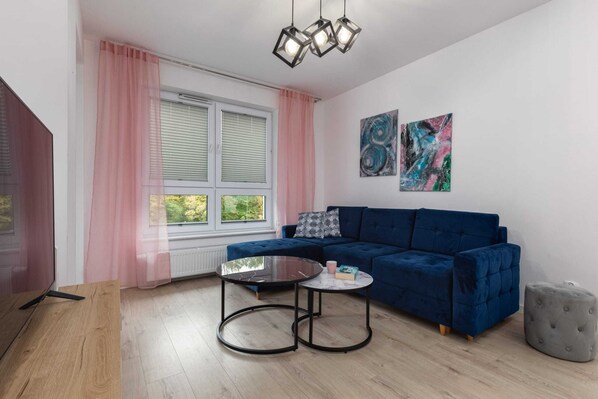 A cozy living room with a stylish blue sofa, pink curtains, and modern decor, creating a warm and inviting space.
