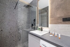 A sleek bathroom with a modern walk-in shower, concrete-style tiles, and complimentary toiletries.
