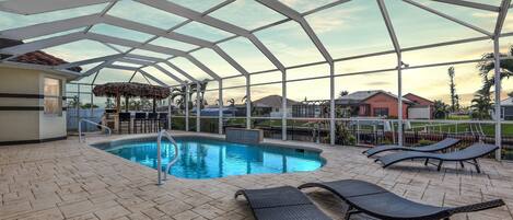 Electric heated pool surrounded by sun loungers and a tiki hut