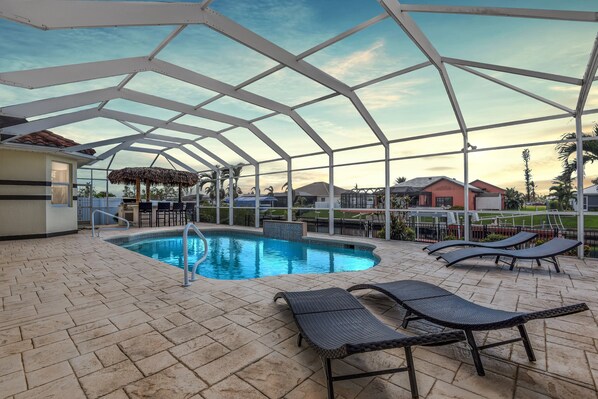 Electric heated pool surrounded by sun loungers and a tiki hut