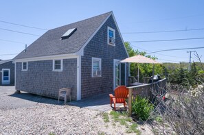 Front of the home with a deck, seating and grill.