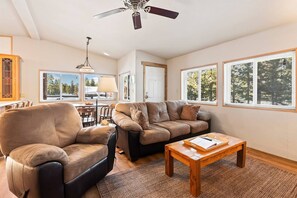 Step into the Ponderosa Pine cabin's welcoming living room, where the entrance seamlessly leads to a charming dining area in the background, creating a fluid and inviting space for relaxation and shared meals.