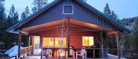Embrace the enchanting twilight ambiance as Valley Creek Cabin's covered patio beckons with a cozy fire pit and convenient gas BBQ, perfect for evening gatherings.