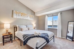 Relax in this serene bedroom featuring a comfortable bed, soft lighting, and a large window that fills the space with natural light.