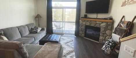 Open living area with natural light, mounted TV & gas fireplace. Walk-out patio.
