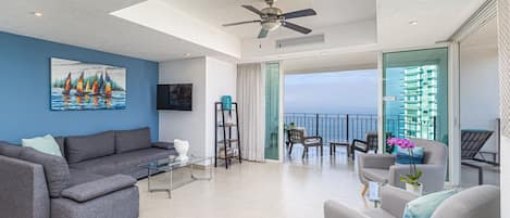 Living room with doors that open completely onto balcony overlooking ocean.