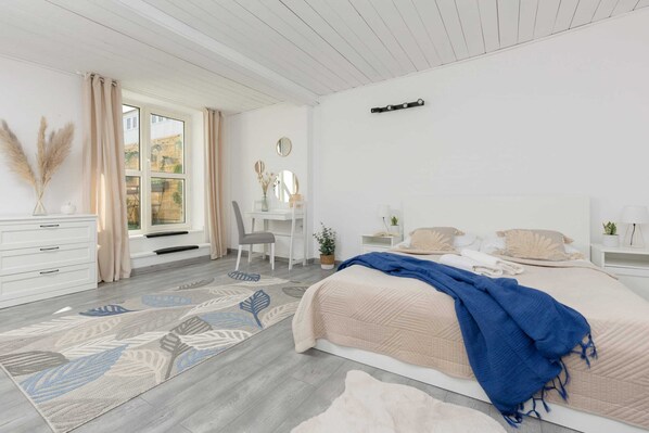 A spacious and bright bedroom featuring a comfortable double bed with blue bedding, a stylish rug, and light decor for a relaxing ambiance.