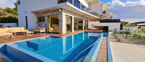 View of the outdoor terrace with seating and sun loungers next to the private heated pool in the luxury villa in Rogoznica