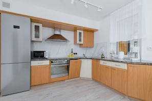 A fully equipped kitchen with light wood cabinets, white countertops, and modern appliances, connected to the dining area.
