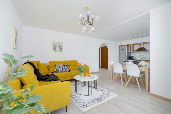 A bright and modern living room with a vibrant yellow sofa, a white coffee table, and contemporary decor creating a cozy atmosphere.