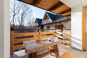 A charming balcony with a wooden table and chairs, surrounded by wooden railings and nature in the background.