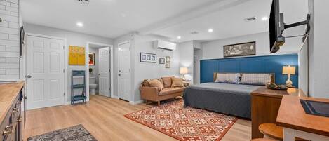 A view of the living area with king size bed, bar height desk/table, a cozy couch for two and a chest of drawers.  There is a 43" smart TV and a mini split heating/cooling system to keep the place comfortable for you. 