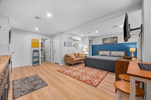 A view of the living area with king size bed, bar height desk/table, a cozy couch for two and a chest of drawers.  There is a 43" smart TV and a mini split heating/cooling system to keep the place comfortable for you. 