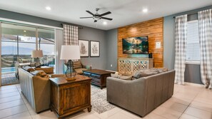 Cozy living area with plush leather seating, rustic accents, large TV, and poolside patio access.