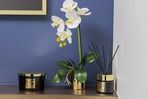A close-up of a decorative setup with a white orchid in a gold planter, placed on a shelf or table.