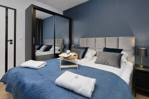A bedroom with a double bed dressed in blue bedding, matching curtains, and bedside tables with lamps.