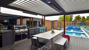 Outdoor Kitchen with Weber BBQ, 5-burner stove and large gas oven, food prep area with deep sink, and bar fridges.