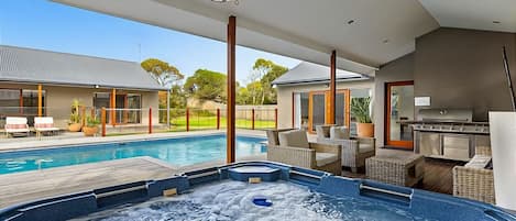 Solar heated swimming pool and hot tub spa beside a sundrenched deck and sheltered alfresco dining with gas mains BBQ, sun umbrella, and outdoor living area. 