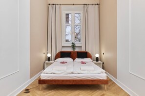 A bedroom with a neatly made double bed, white bedding, and a decorative red bow placed on the bed for a welcoming touch.