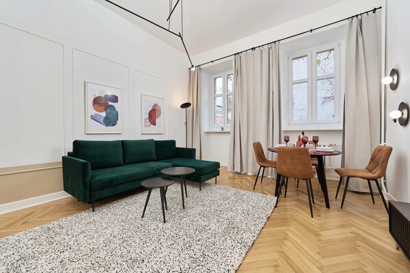 A cozy living room with a green sofa, a round coffee table, and a modern rug on wooden flooring, complemented by natural light from the windows.