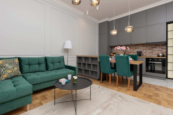 A modern dining area with a wooden table, green upholstered chairs, and a cozy corner sofa.