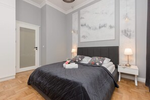A cozy bedroom with a neatly made bed covered in gray bedding, side lamps, and a minimalist design.