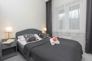 A serene bedroom featuring gray curtains, a cozy bed, and warm bedside lighting.