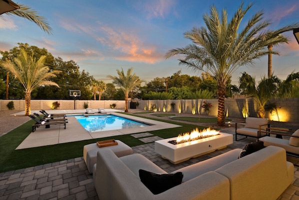 Cuddle up with friends and family in this backyard oasis with a fire pit, comfortable couches, and swaying palm trees.
