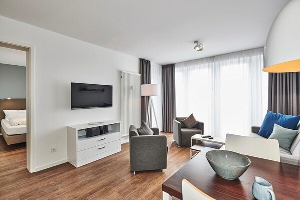 Wohn-Essbereich mit Couch, Flatscreen TV, Esstisch, Sitzgelegenheit und Zugang zum Balkon